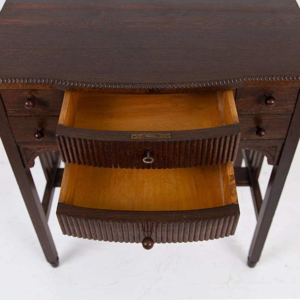 A 1930s Art Deco dark oak side table featuring six small drawers with fluted fronts and turned wooden handles, supported by tall legs and an H-stretcher. View IV