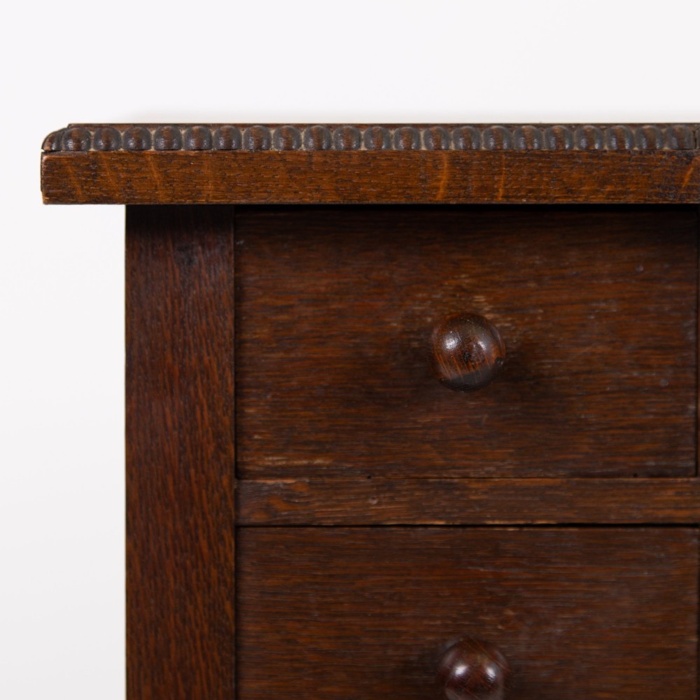 A 1930s Art Deco dark oak side table featuring six small drawers with fluted fronts and turned wooden handles, supported by tall legs and an H-stretcher. View V