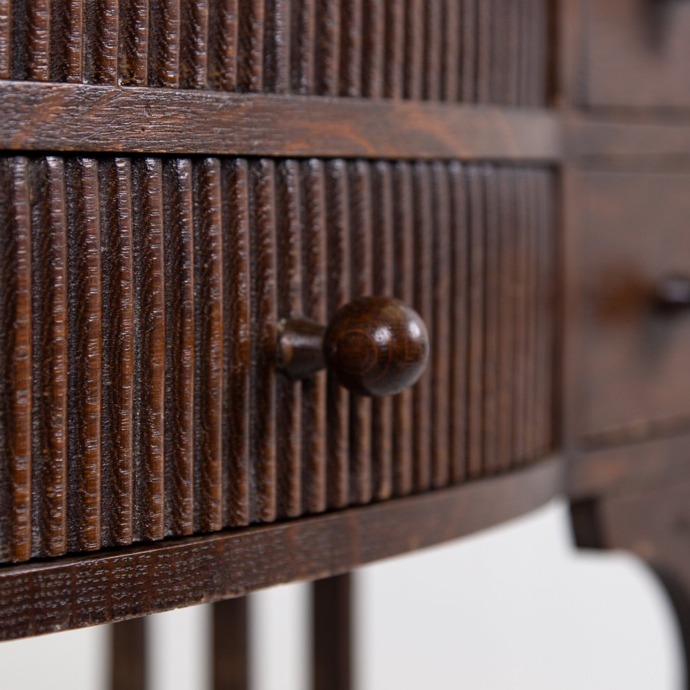 A 1930s Art Deco dark oak side table featuring six small drawers with fluted fronts and turned wooden handles, supported by tall legs and an H-stretcher. View VI