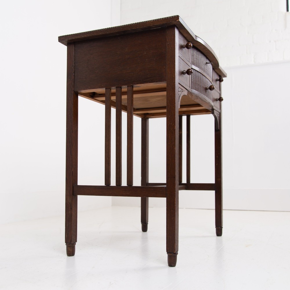 A 1930s Art Deco dark oak side table featuring six small drawers with fluted fronts and turned wooden handles, supported by tall legs and an H-stretcher. View VIII