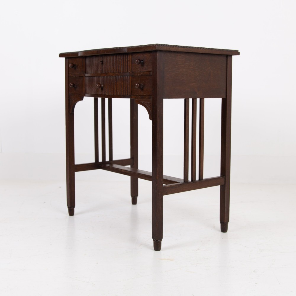 A 1930s Art Deco dark oak side table featuring six small drawers with fluted fronts and turned wooden handles, supported by tall legs and an H-stretcher. View XII