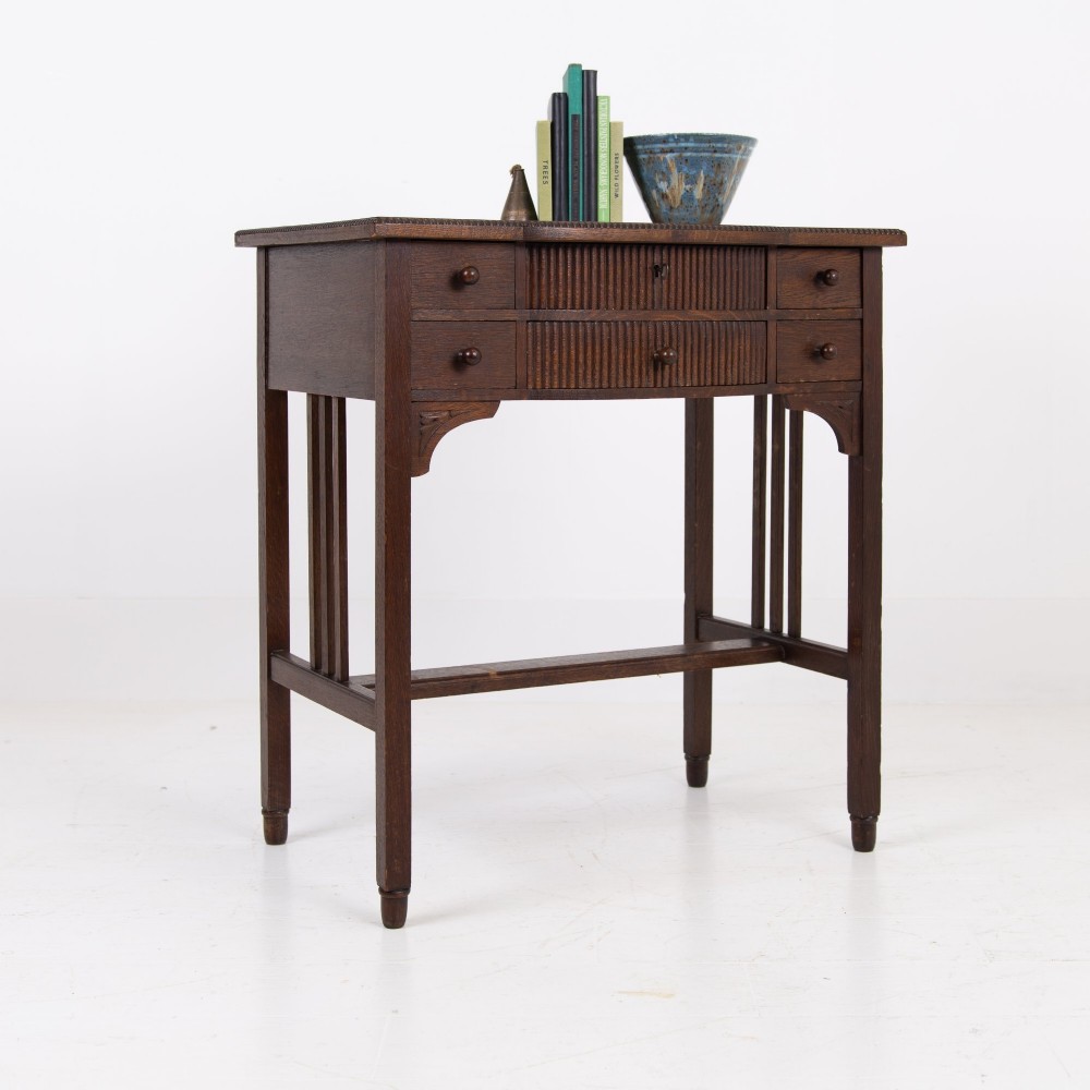 A 1930s Art Deco dark oak side table featuring six small drawers with fluted fronts and turned wooden handles, supported by tall legs and an H-stretcher. View XIII