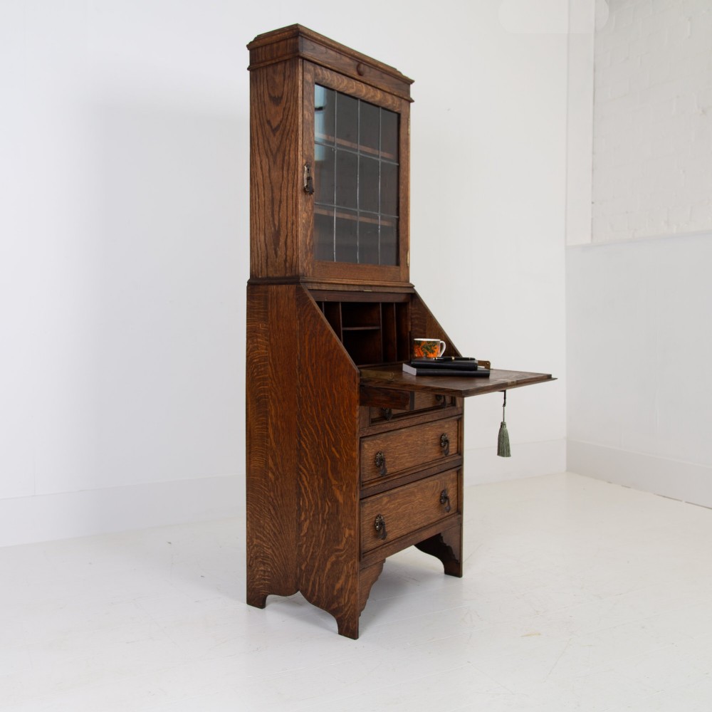 A small early 20th-century oak bureau bookcase featuring a leaded glass upper cabinet, a slant-front writing slope, and three lower drawers with brass drop handles. View III