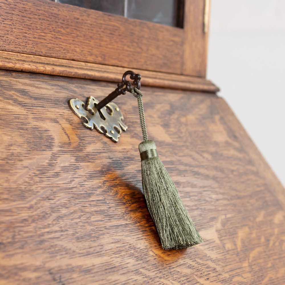 A small early 20th-century oak bureau bookcase featuring a leaded glass upper cabinet, a slant-front writing slope, and three lower drawers with brass drop handles. View IV
