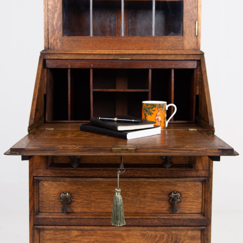A small early 20th-century oak bureau bookcase featuring a leaded glass upper cabinet, a slant-front writing slope, and three lower drawers with brass drop handles. View V