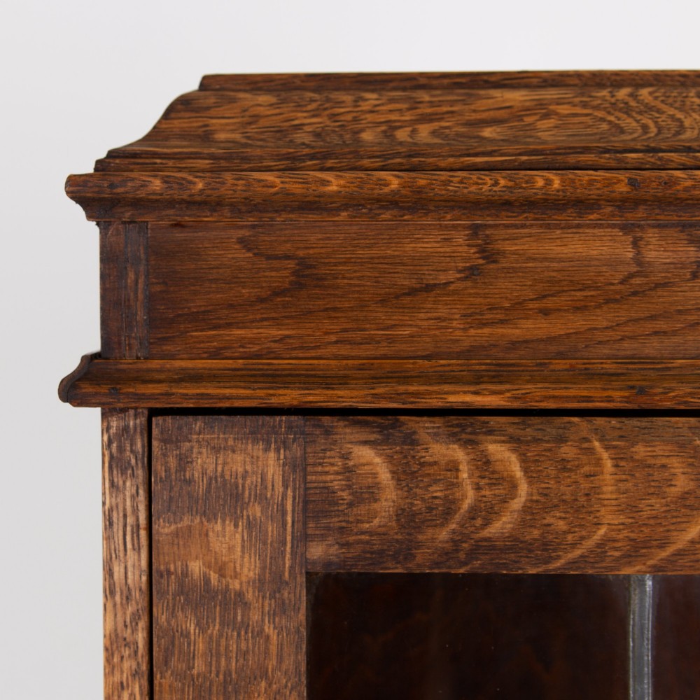 A small early 20th-century oak bureau bookcase featuring a leaded glass upper cabinet, a slant-front writing slope, and three lower drawers with brass drop handles. View VIII