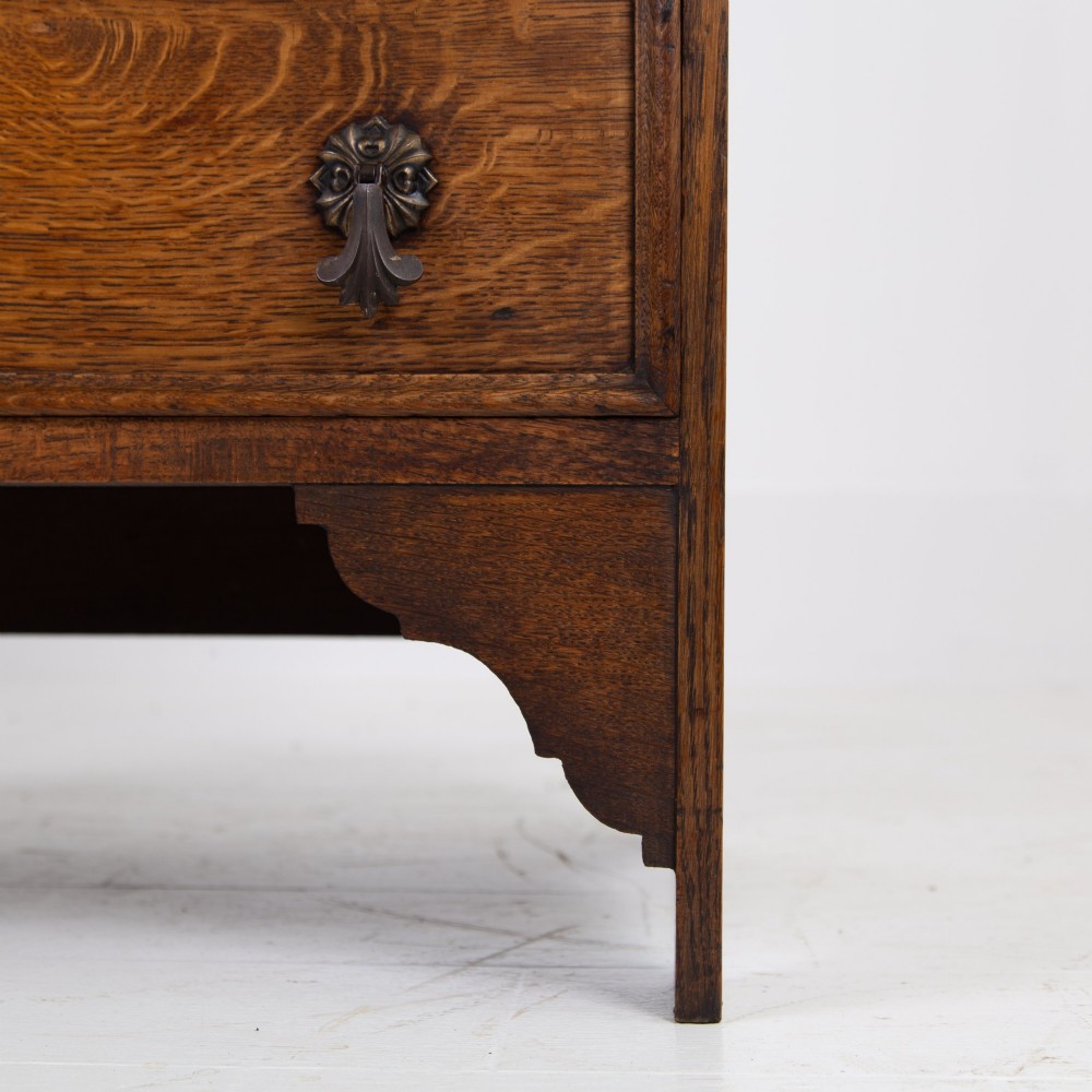 A small early 20th-century oak bureau bookcase featuring a leaded glass upper cabinet, a slant-front writing slope, and three lower drawers with brass drop handles. View X