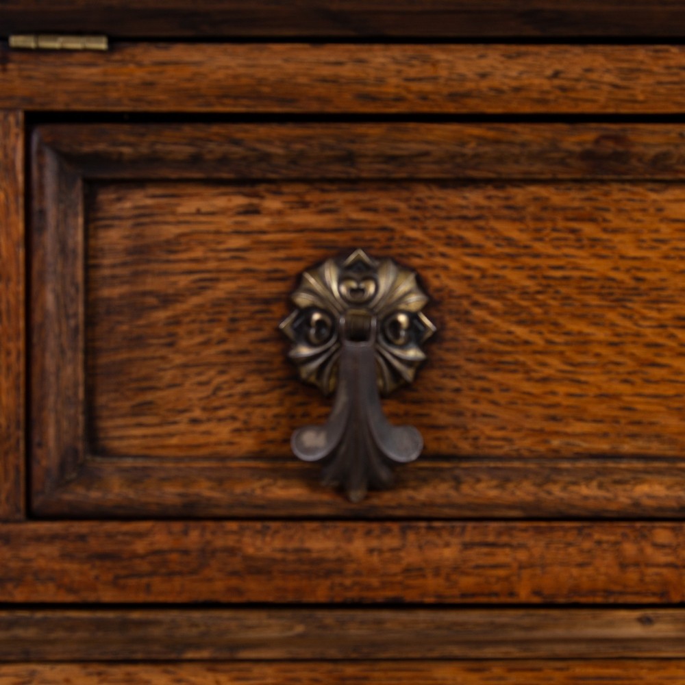 A small early 20th-century oak bureau bookcase featuring a leaded glass upper cabinet, a slant-front writing slope, and three lower drawers with brass drop handles. View XI