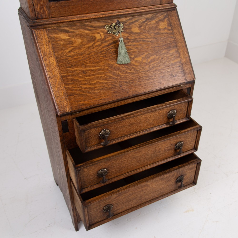 A small early 20th-century oak bureau bookcase featuring a leaded glass upper cabinet, a slant-front writing slope, and three lower drawers with brass drop handles. View XII