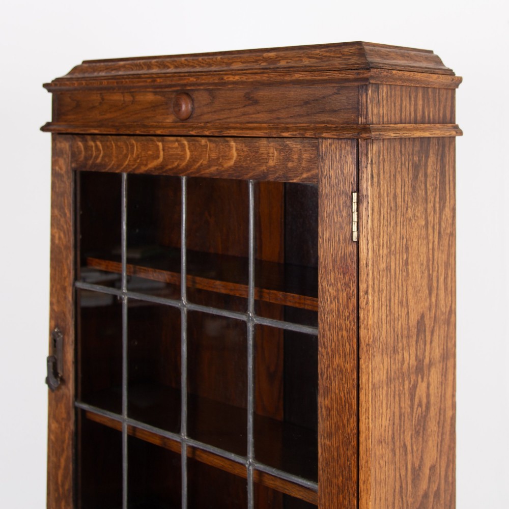 A small early 20th-century oak bureau bookcase featuring a leaded glass upper cabinet, a slant-front writing slope, and three lower drawers with brass drop handles. View XIV