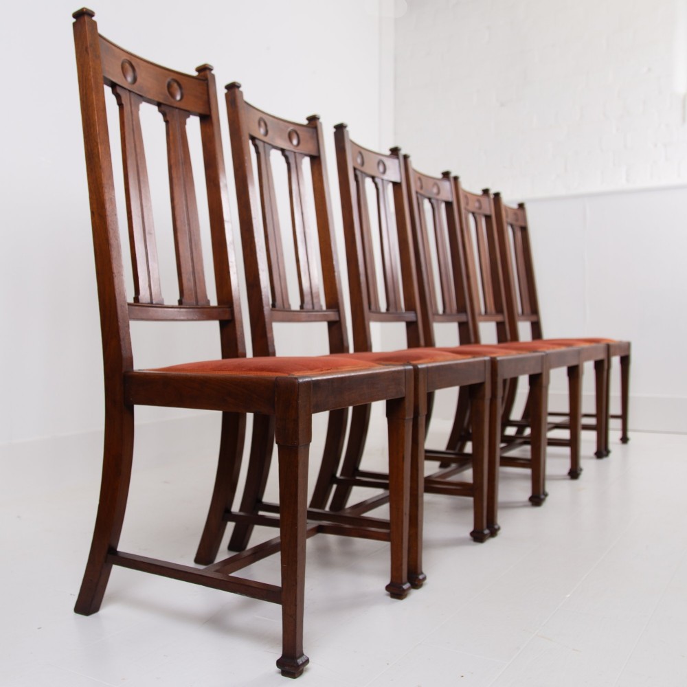 A set of six Scottish Arts and Crafts oak dining chairs featuring high slatted backs with carved roundel details and red velvet seat pads. View II
