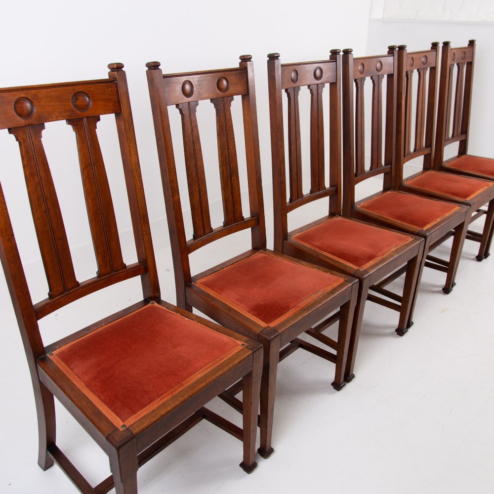 A set of six Scottish Arts and Crafts oak dining chairs featuring high slatted backs with carved roundel details and red velvet seat pads. View IV