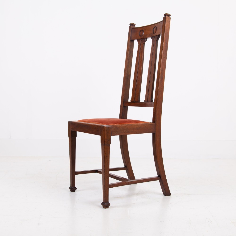 A set of six Scottish Arts and Crafts oak dining chairs featuring high slatted backs with carved roundel details and red velvet seat pads. View V
