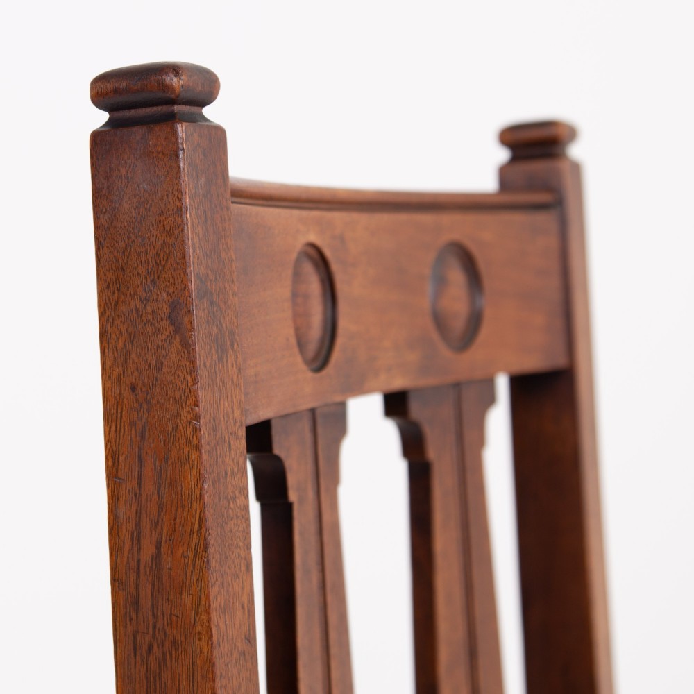A set of six Scottish Arts and Crafts oak dining chairs featuring high slatted backs with carved roundel details and red velvet seat pads. View VI