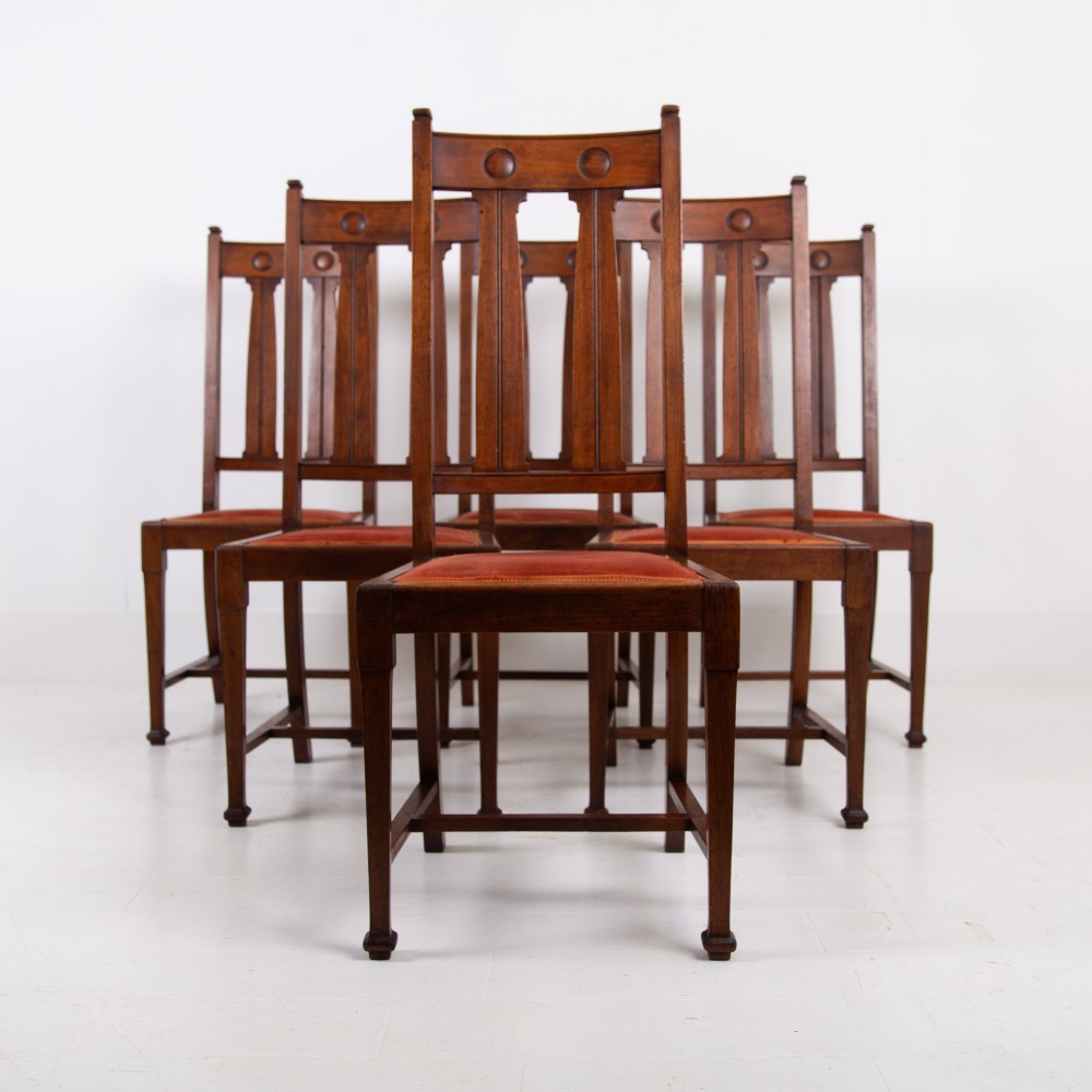 A set of six Scottish Arts and Crafts oak dining chairs featuring high slatted backs with carved roundel details and red velvet seat pads. View XIV