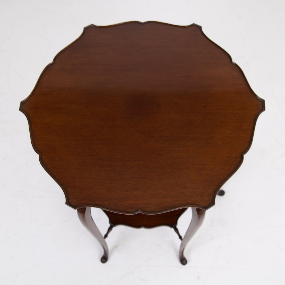 An Edwardian mahogany occasional side table featuring a scalloped rim top, slender cabriole legs, and a matching lower undertier shelf. View X