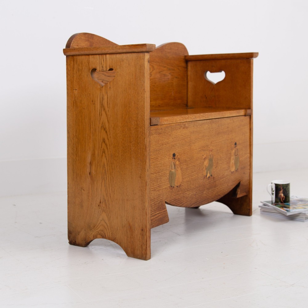 An Arts and Crafts solid oak box settle featuring heart cut-out side panels, an arched backrest, and figural wood inlay on the front apron.