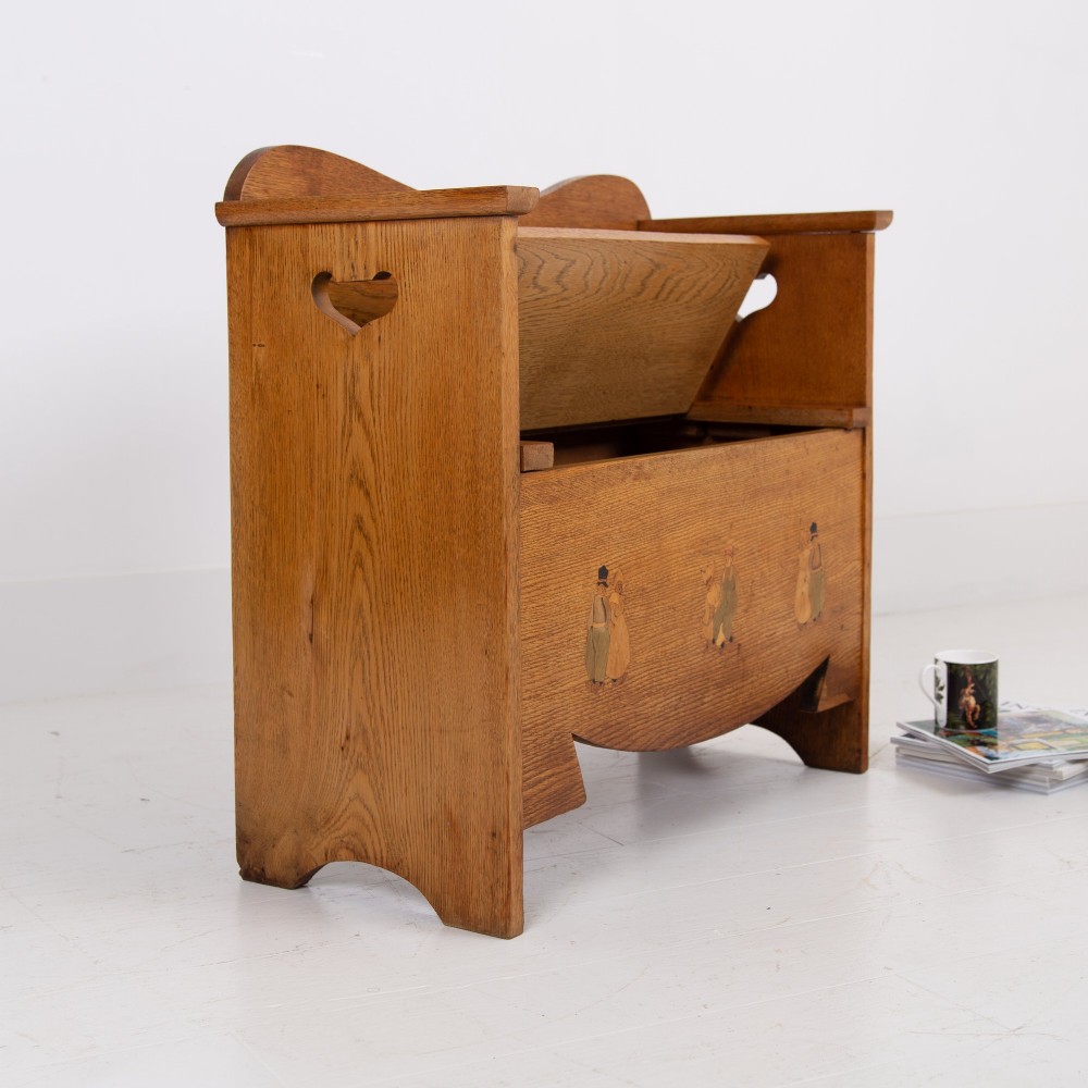 An Arts and Crafts solid oak box settle featuring heart cut-out side panels, an arched backrest, and figural wood inlay on the front apron. View II