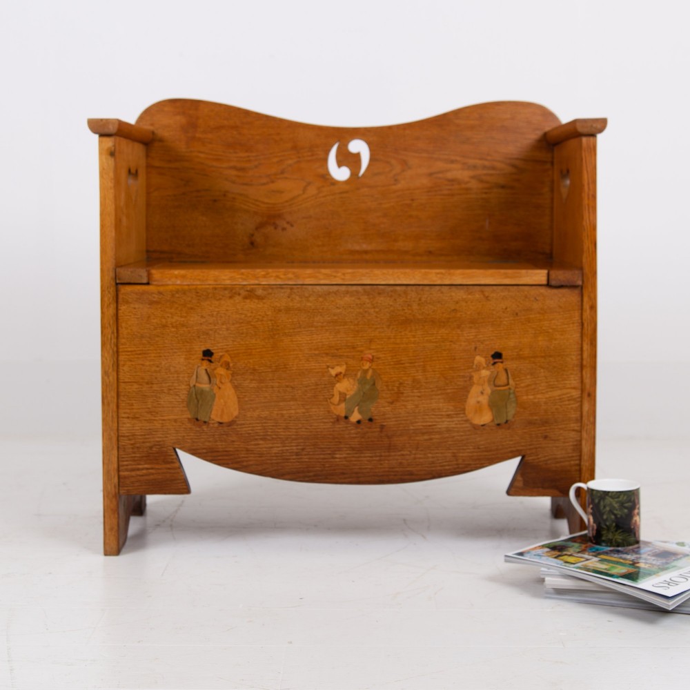 An Arts and Crafts solid oak box settle featuring heart cut-out side panels, an arched backrest, and figural wood inlay on the front apron. View III