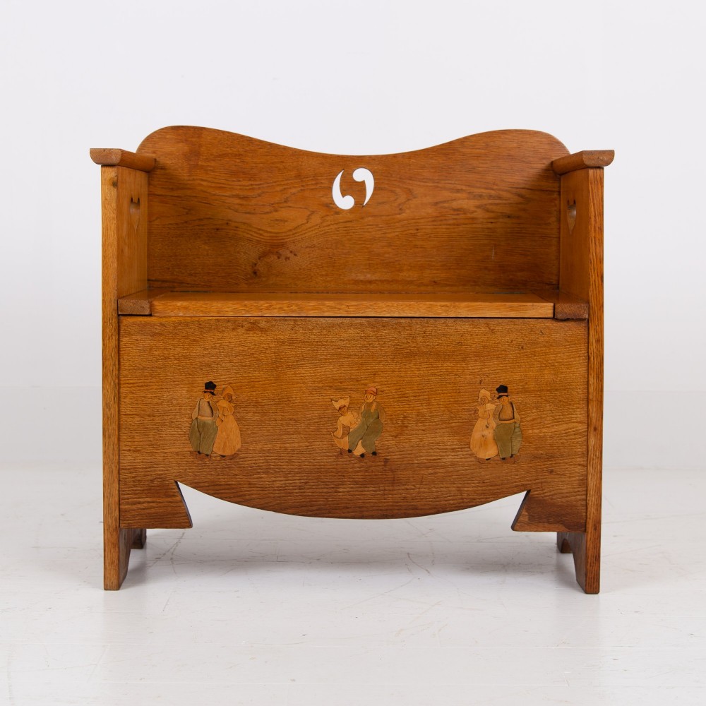 An Arts and Crafts solid oak box settle featuring heart cut-out side panels, an arched backrest, and figural wood inlay on the front apron. View VI