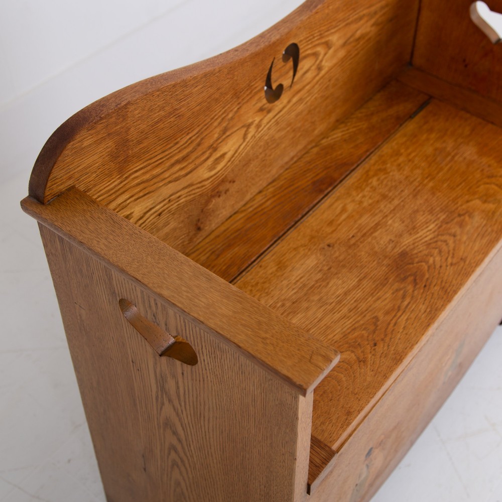 An Arts and Crafts solid oak box settle featuring heart cut-out side panels, an arched backrest, and figural wood inlay on the front apron. View XI
