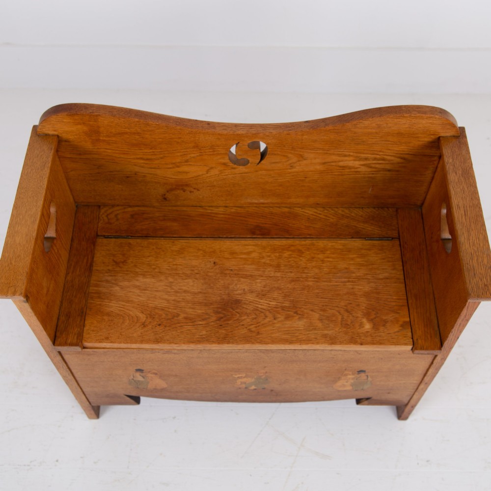 An Arts and Crafts solid oak box settle featuring heart cut-out side panels, an arched backrest, and figural wood inlay on the front apron. View XIII