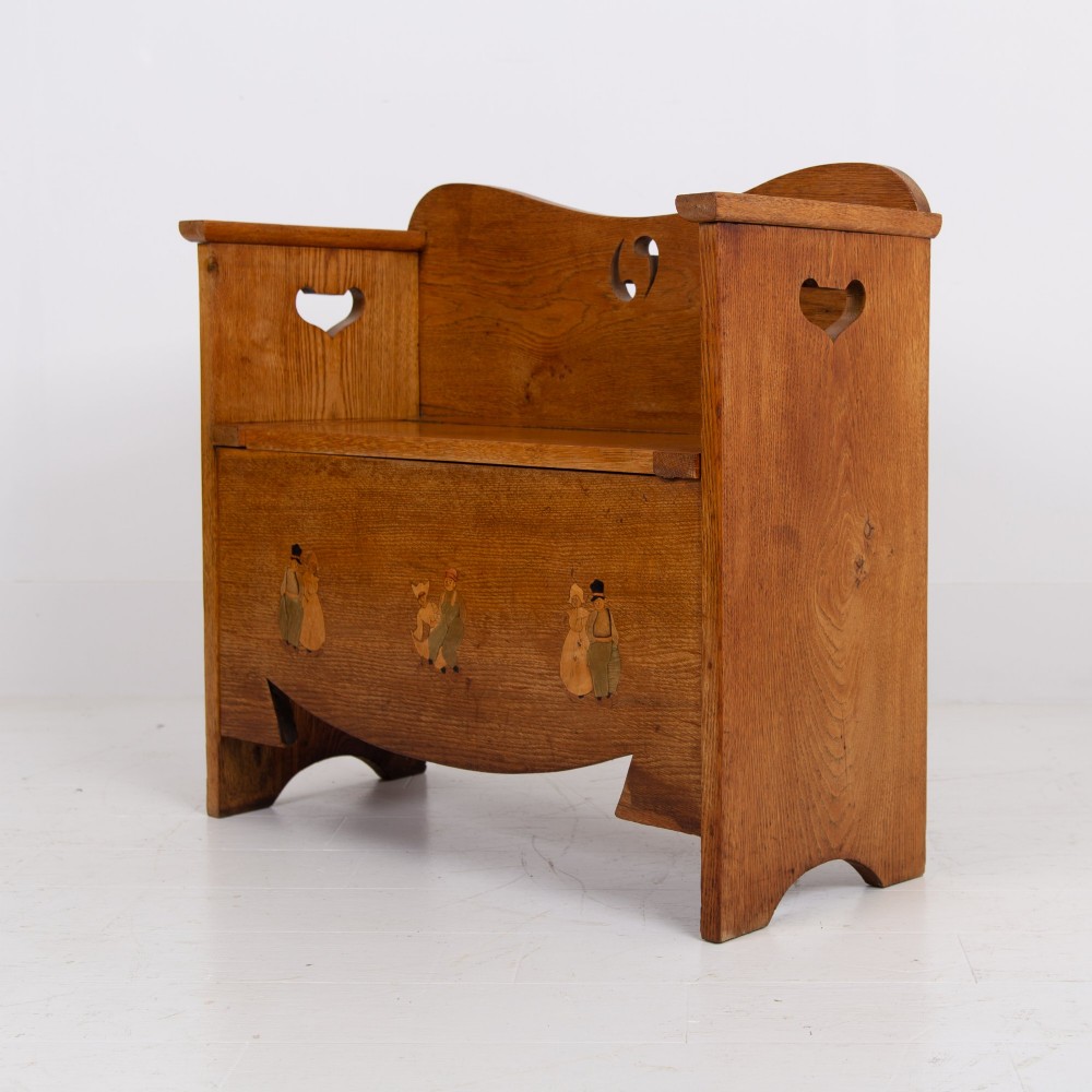 An Arts and Crafts solid oak box settle featuring heart cut-out side panels, an arched backrest, and figural wood inlay on the front apron. View XIV