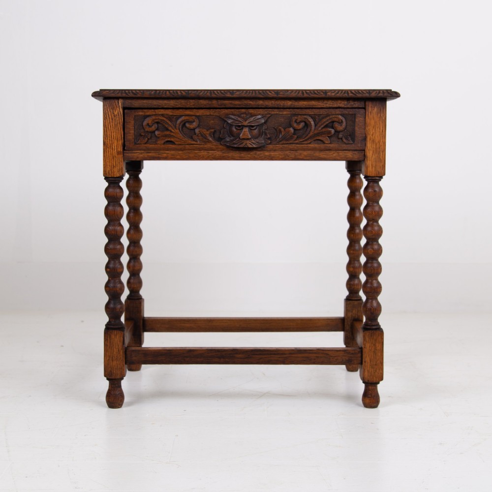 A dark oak Victorian side table featuring a single drawer carved with a Green Man mask motif, bobbin-turned legs, and a lower rectangular stretcher. View II