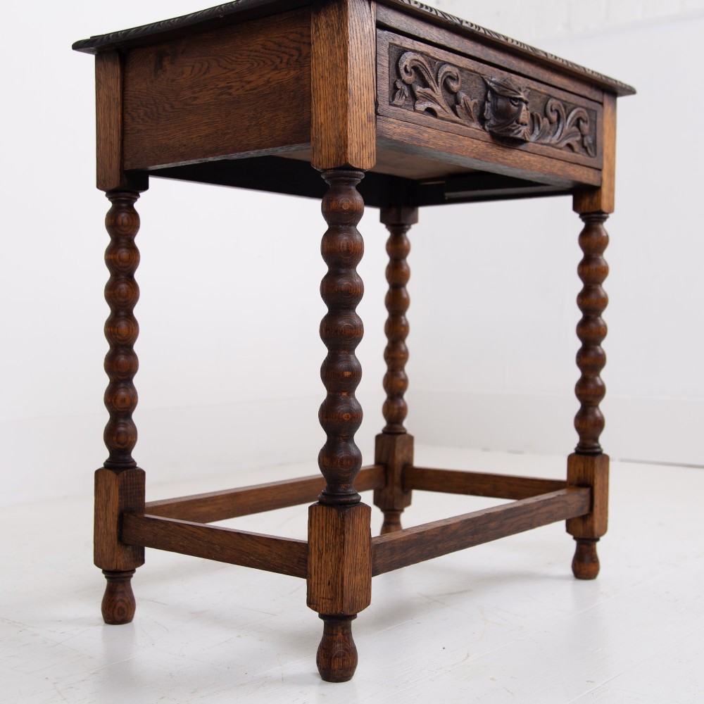 A dark oak Victorian side table featuring a single drawer carved with a Green Man mask motif, bobbin-turned legs, and a lower rectangular stretcher. View VIII