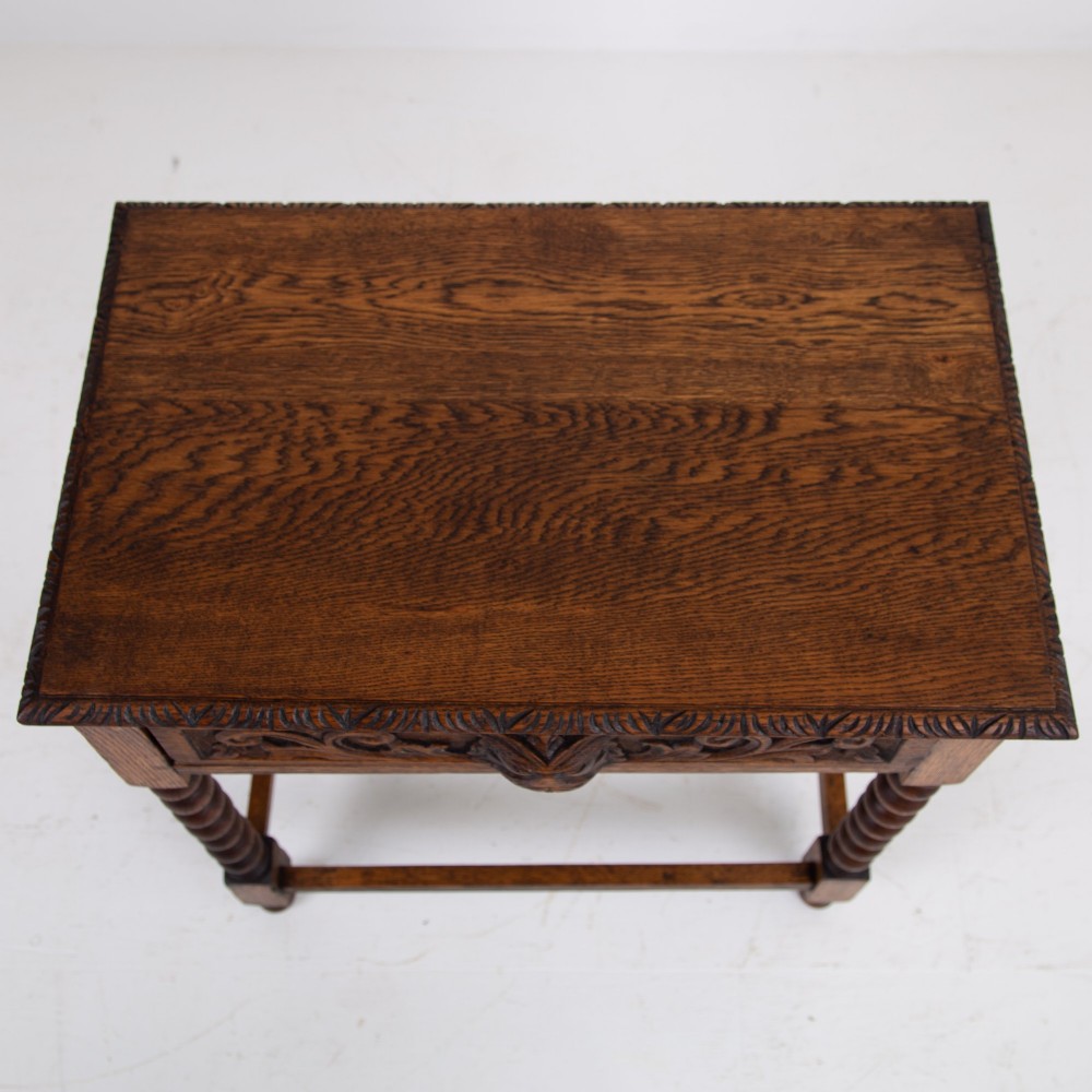 A dark oak Victorian side table featuring a single drawer carved with a Green Man mask motif, bobbin-turned legs, and a lower rectangular stretcher. View IX