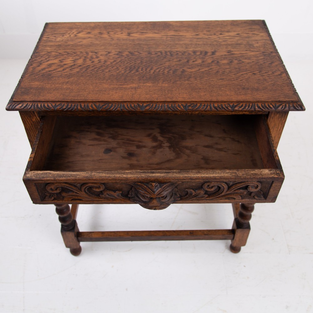 A dark oak Victorian side table featuring a single drawer carved with a Green Man mask motif, bobbin-turned legs, and a lower rectangular stretcher. View XII
