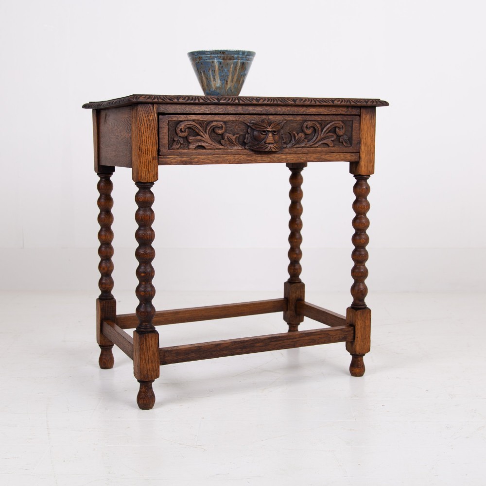A dark oak Victorian side table featuring a single drawer carved with a Green Man mask motif, bobbin-turned legs, and a lower rectangular stretcher. View XIII