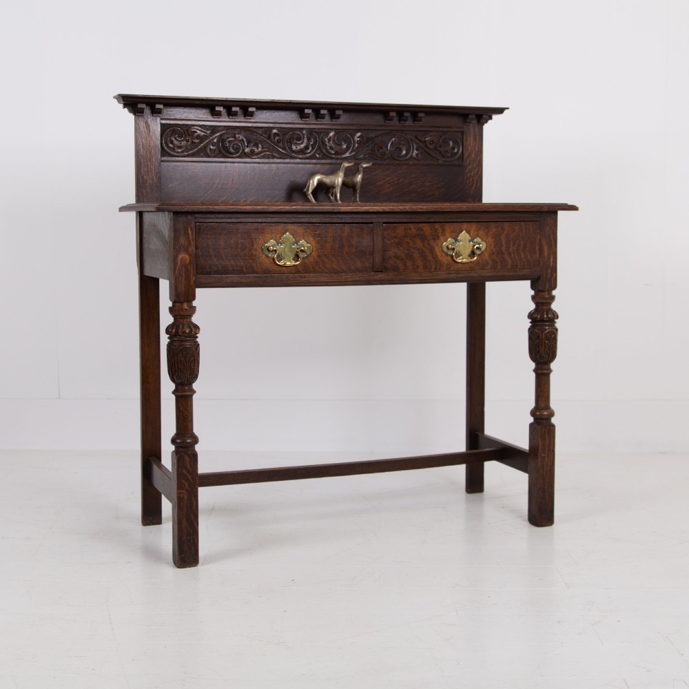 A dark oak console hall table featuring a carved back gallery, two drawers with brass backplate handles, and turned front legs.