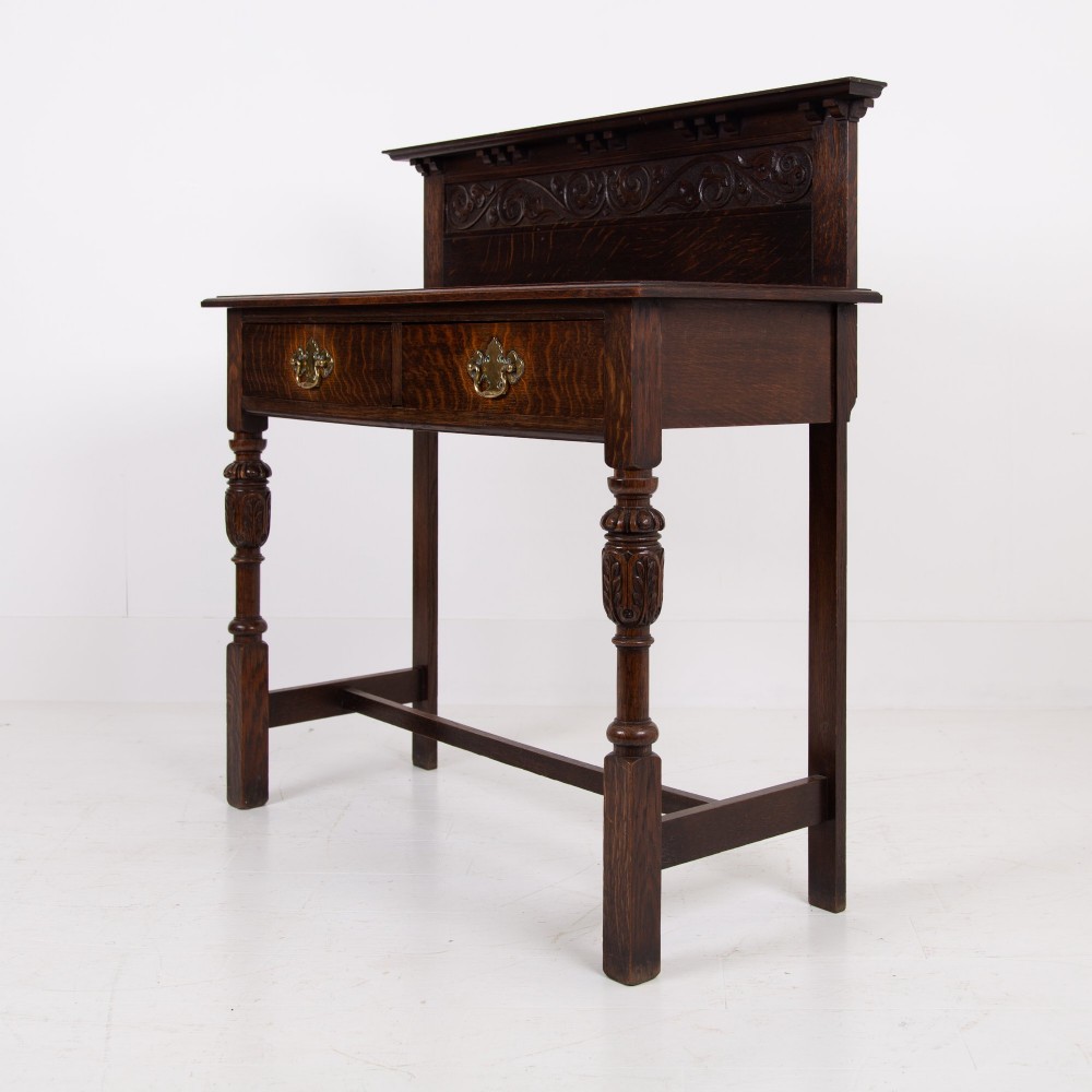 A dark oak console hall table featuring a carved back gallery, two drawers with brass backplate handles, and turned front legs. View II