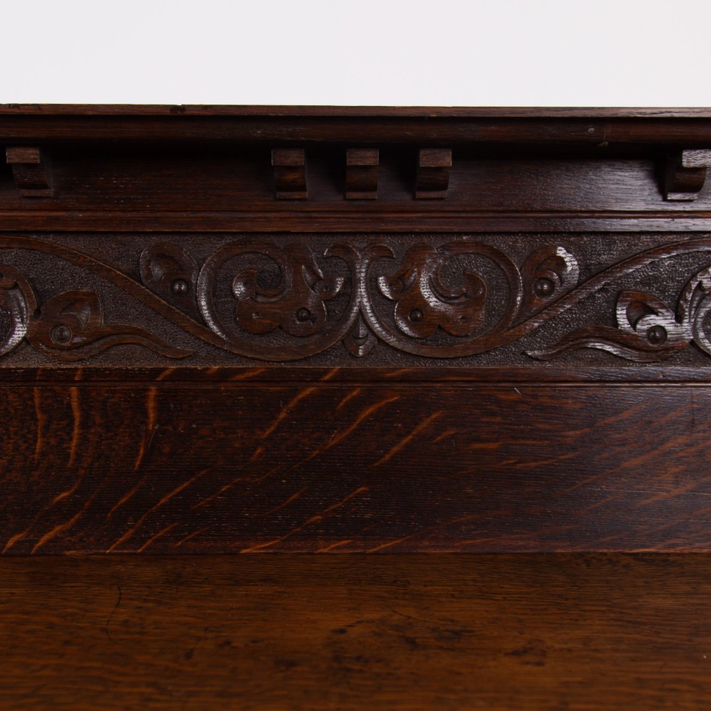 A dark oak console hall table featuring a carved back gallery, two drawers with brass backplate handles, and turned front legs. View III