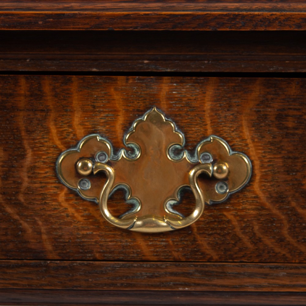 A dark oak console hall table featuring a carved back gallery, two drawers with brass backplate handles, and turned front legs. View V