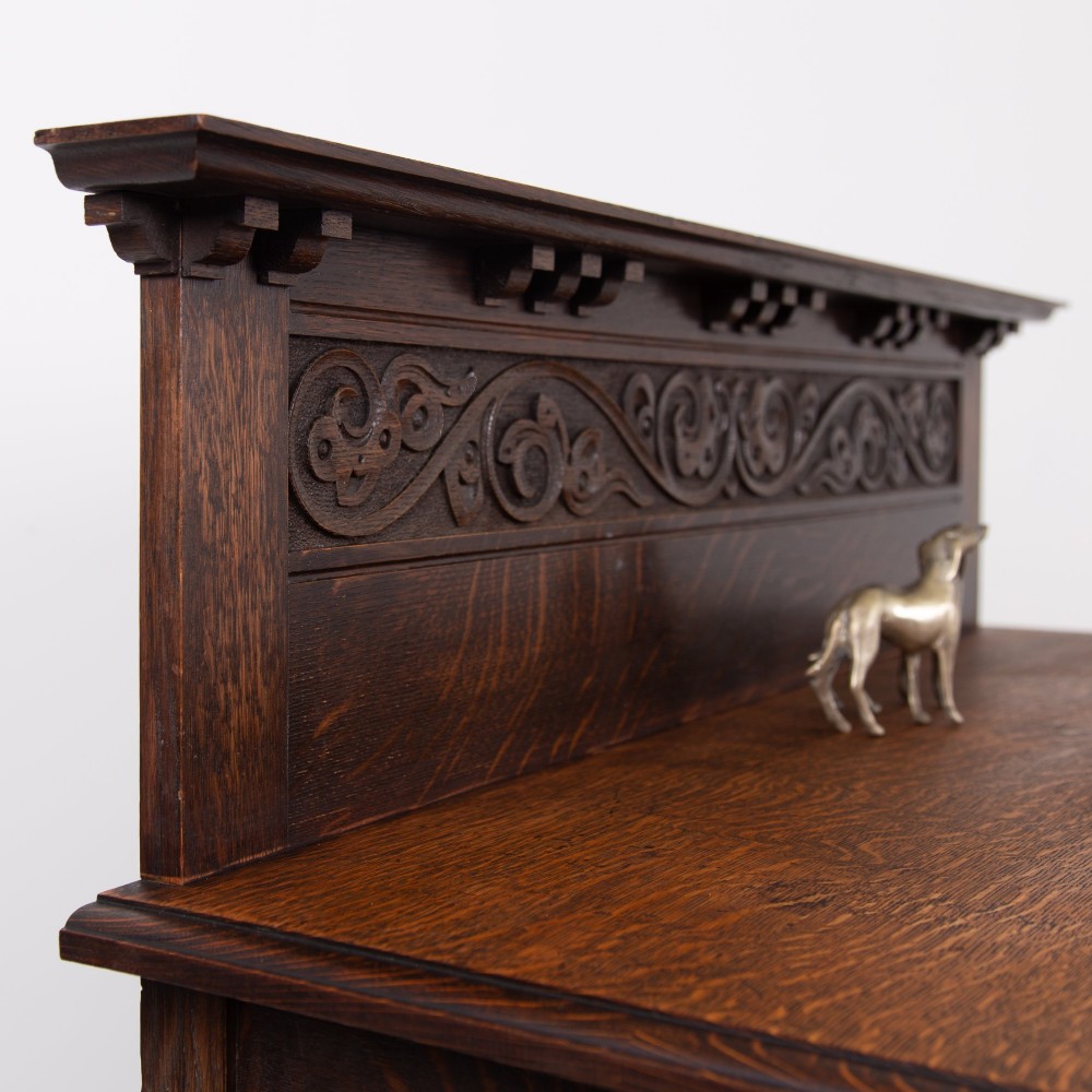 A dark oak console hall table featuring a carved back gallery, two drawers with brass backplate handles, and turned front legs. View VI
