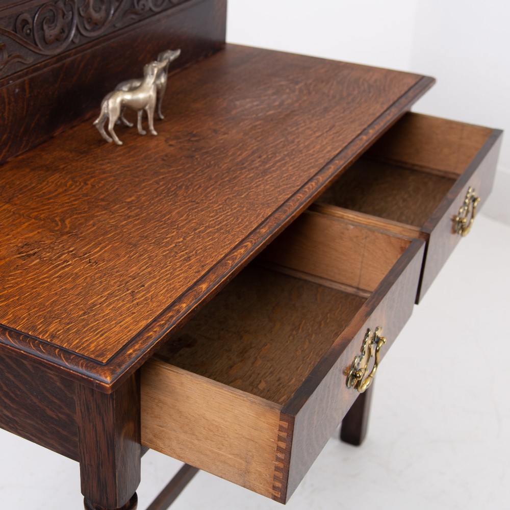 A dark oak console hall table featuring a carved back gallery, two drawers with brass backplate handles, and turned front legs. View VIII