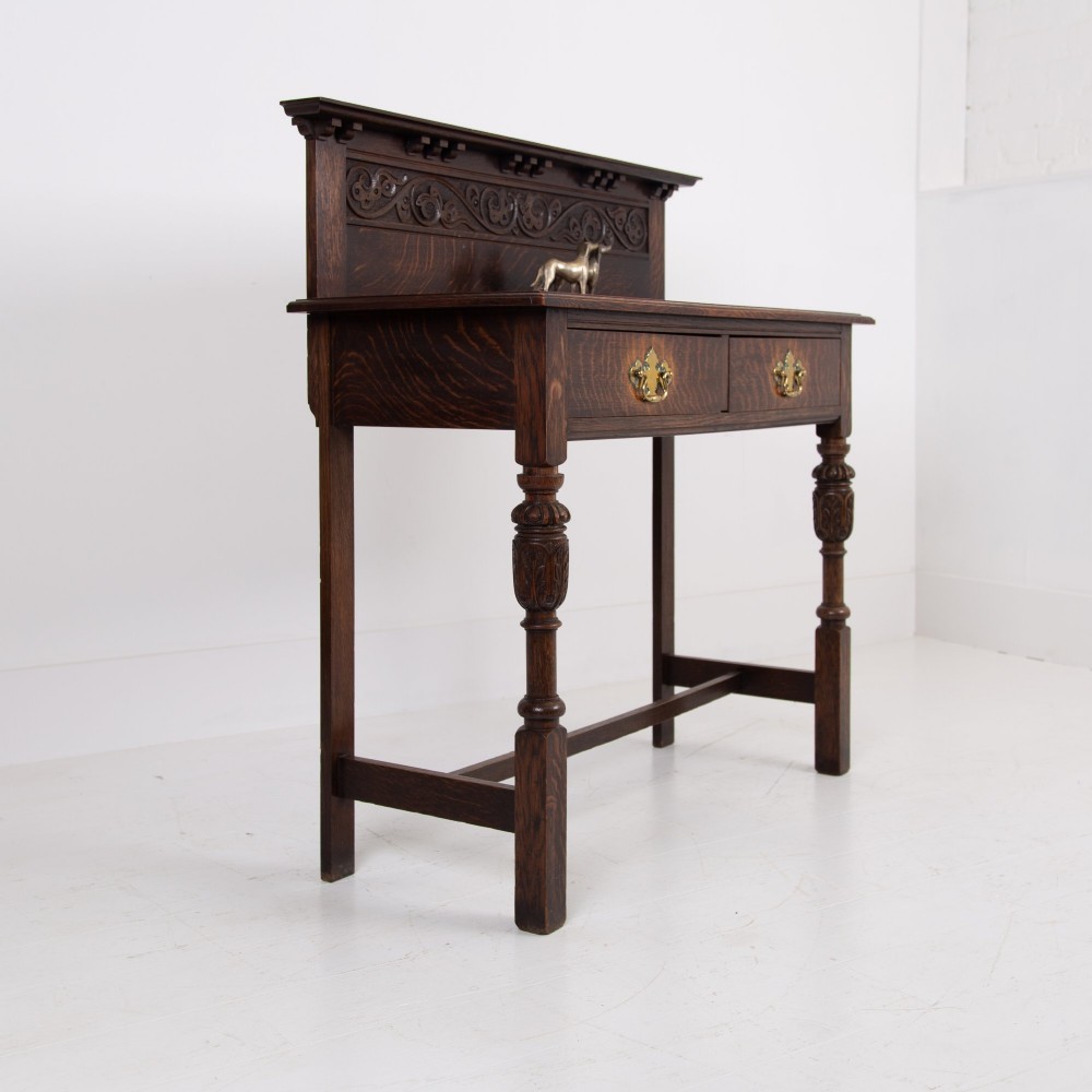 A dark oak console hall table featuring a carved back gallery, two drawers with brass backplate handles, and turned front legs. View IX