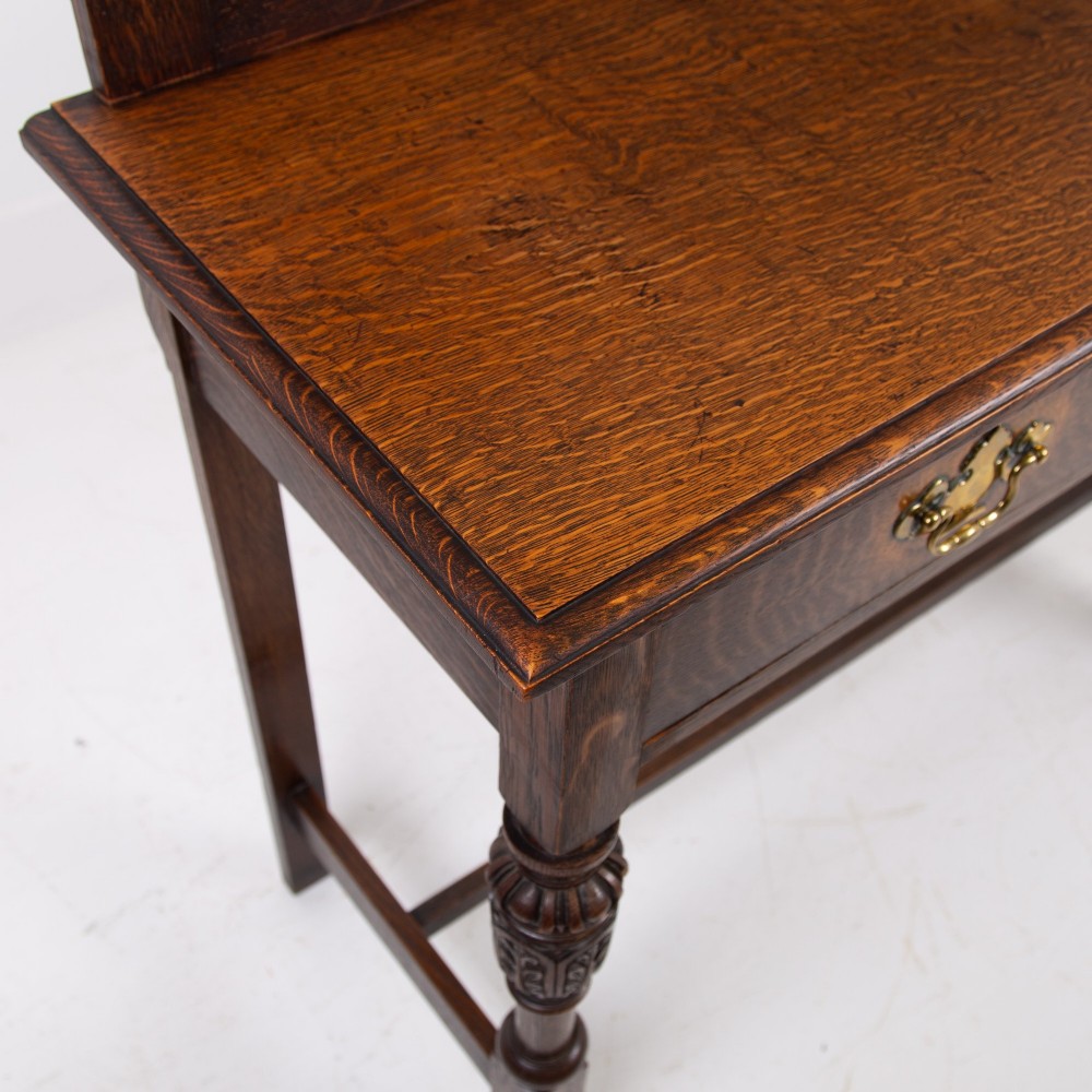A dark oak console hall table featuring a carved back gallery, two drawers with brass backplate handles, and turned front legs. View XII