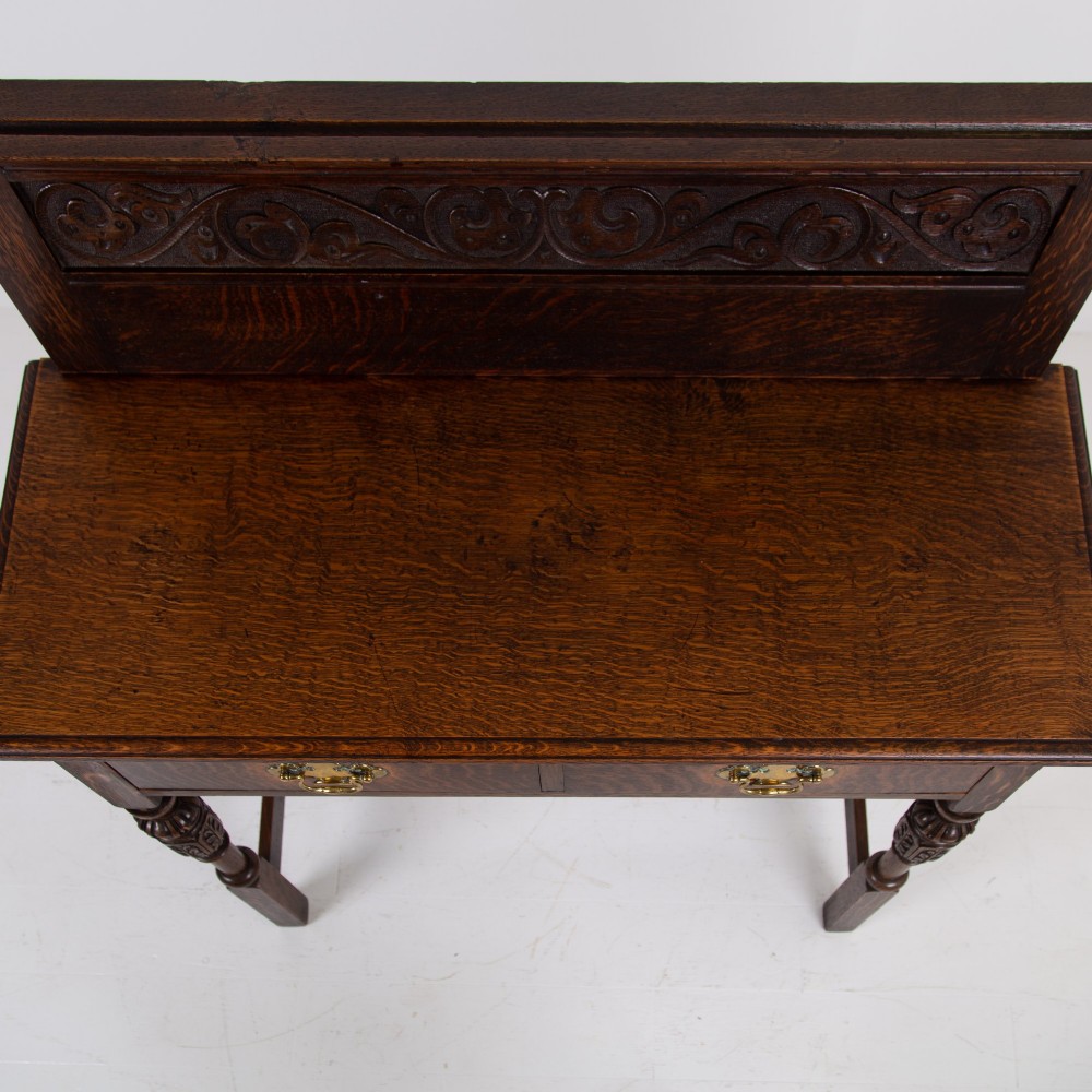 A dark oak console hall table featuring a carved back gallery, two drawers with brass backplate handles, and turned front legs. View XIII