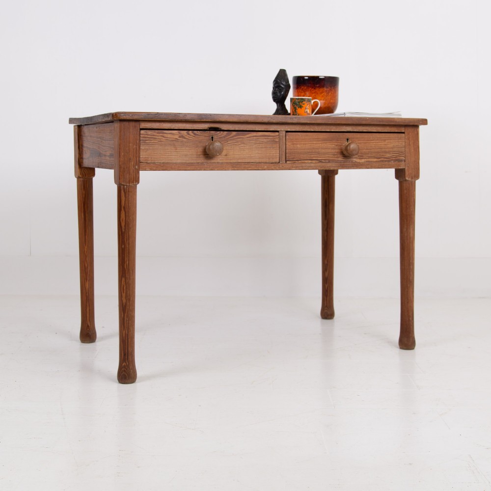 An early 20th-century pitch pine writing desk with two front drawers, wooden turned knobs, and four turned legs.