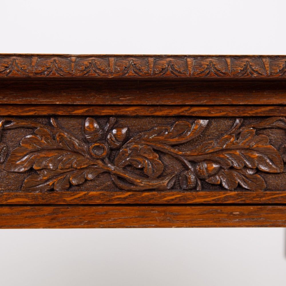 An oak writing desk featuring three carved foliage drawer fronts, bobbin-turned legs, brass drop handles, and a low under-tier shelf. View III