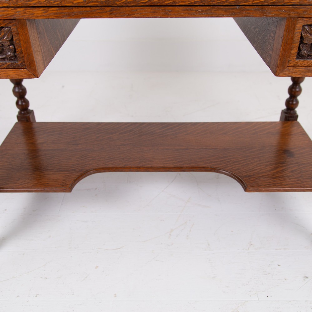 An oak writing desk featuring three carved foliage drawer fronts, bobbin-turned legs, brass drop handles, and a low under-tier shelf. View V