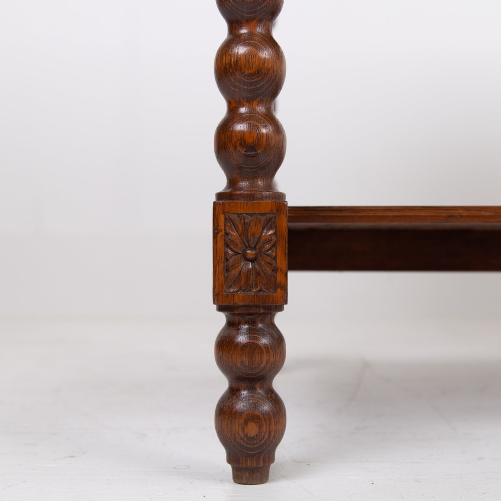 An oak writing desk featuring three carved foliage drawer fronts, bobbin-turned legs, brass drop handles, and a low under-tier shelf. View VI