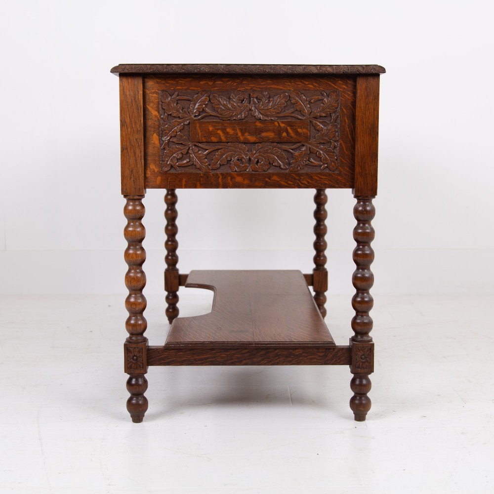 An oak writing desk featuring three carved foliage drawer fronts, bobbin-turned legs, brass drop handles, and a low under-tier shelf. View VIII