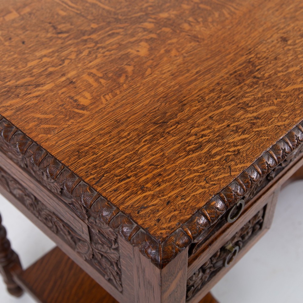 An oak writing desk featuring three carved foliage drawer fronts, bobbin-turned legs, brass drop handles, and a low under-tier shelf. View IX