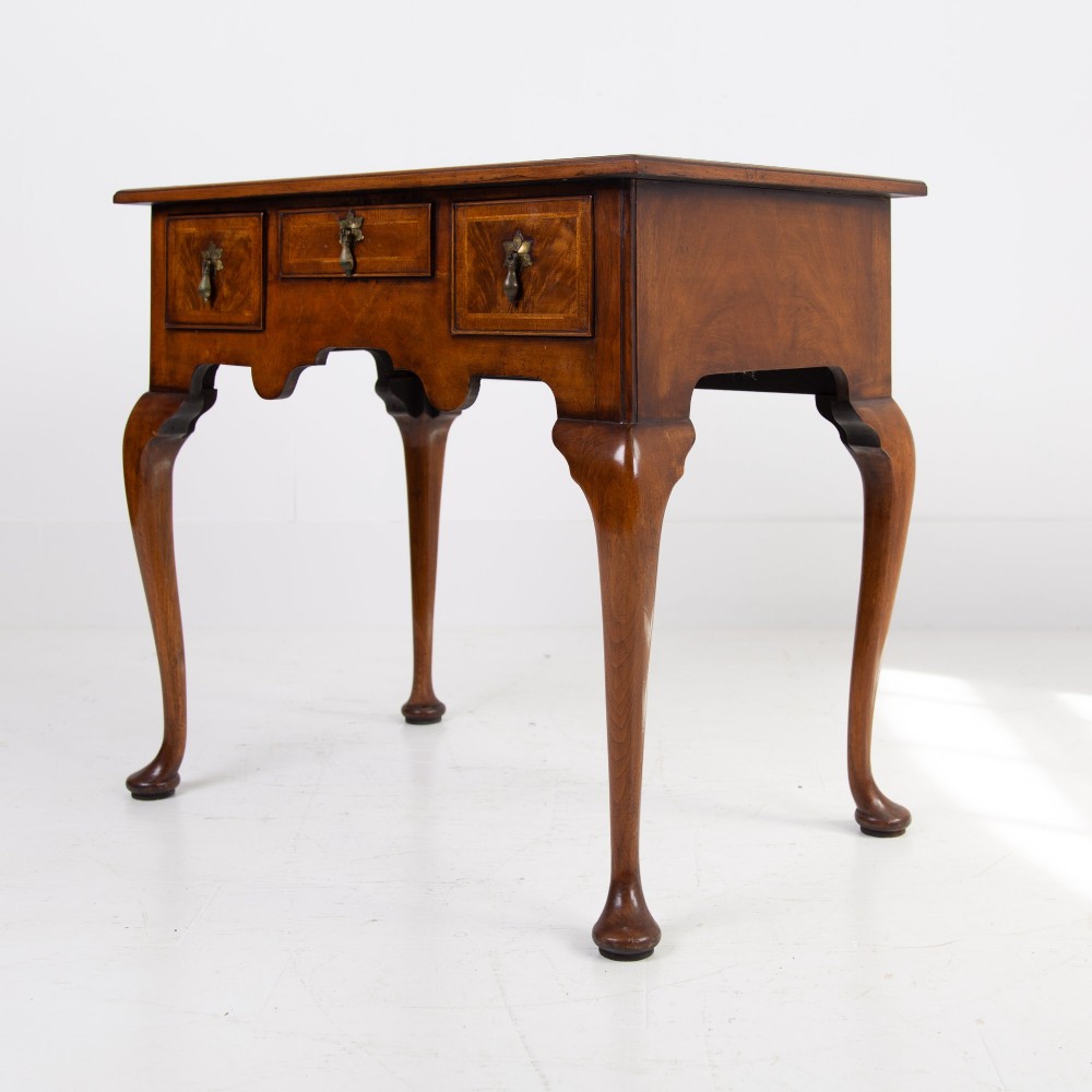 An antique warm brown walnut lowboy table featuring three drawers with brass handles, a shaped apron, and four cabriole legs ending in pad feet.