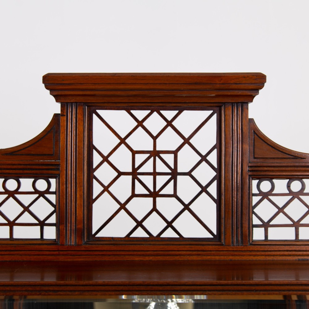 An Aesthetic Movement dark mahogany glazed cabinet with an intricate fretwork upper superstructure, mirrored back, twin glass doors, and a open lower shelf. View III