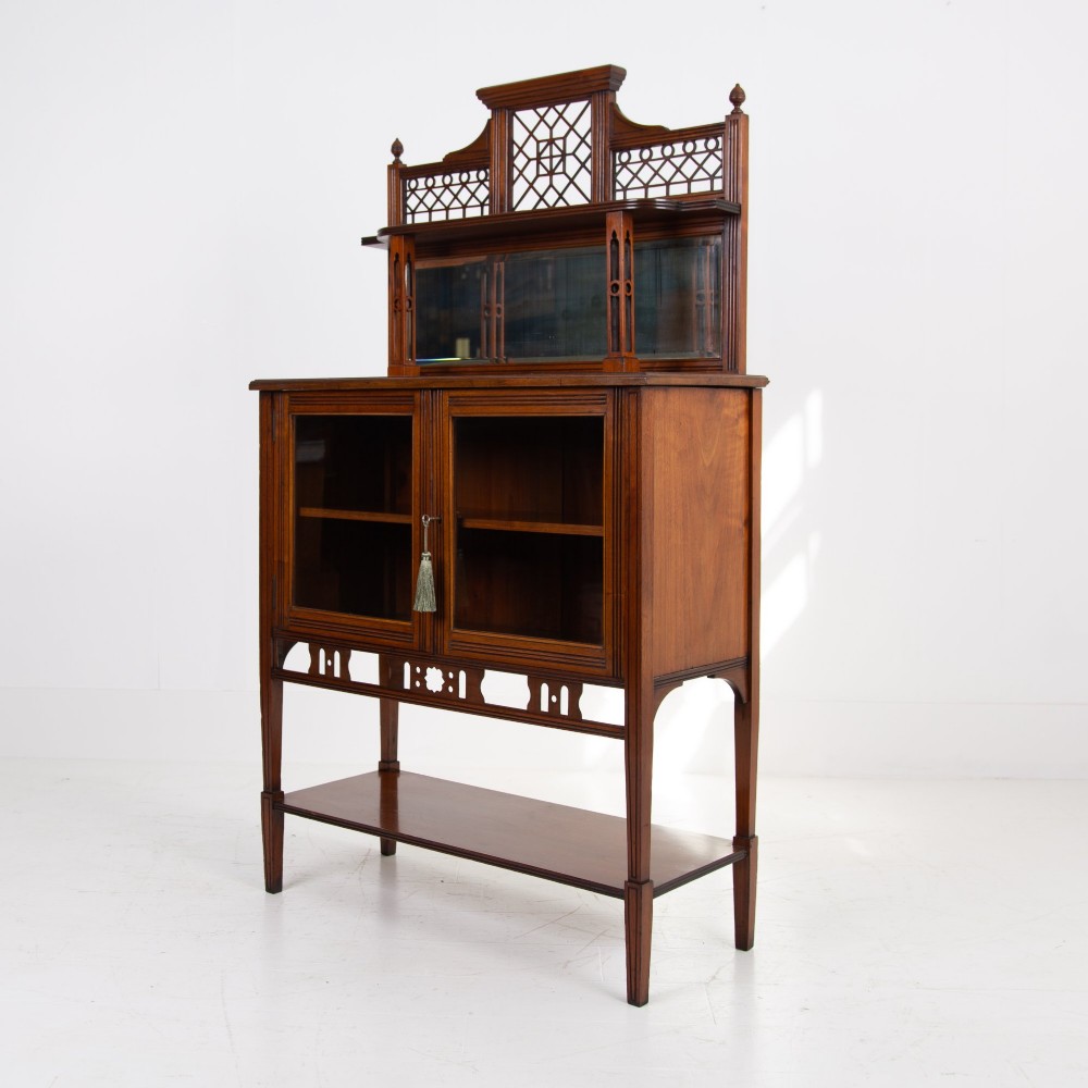 An Aesthetic Movement dark mahogany glazed cabinet with an intricate fretwork upper superstructure, mirrored back, twin glass doors, and a open lower shelf. View XII